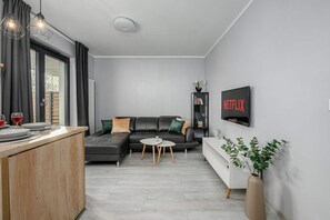 Een moderne woonkamer met een hoekbank, een salontafel, een aan de muur bevestigde televisie, en een eethoek met een houten tafel en stoelen.