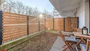 Eine Holzterrasse mit Tisch und Stühlen, ein Holzzaun und ein Gebäude im Hintergrund.