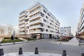 A multi-story residential building with balconies, a paved pedestrian area, and a clear sky. - 2-Bedroom Home with Balcony (Warszawa 2)