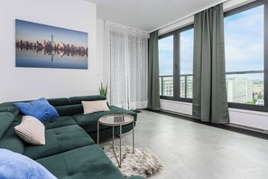 A modern living room with a green sofa, a laptop on a small table, and a cityscape view through large windows. - Warsaw Flat with Balcony (Warszawa)