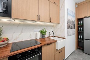 A modern kitchen with wooden cabinets, a black induction cooktop, a stainless steel refrigerator, and a marble backsplash. - Warsaw Flat with Balcony (Warszawa)