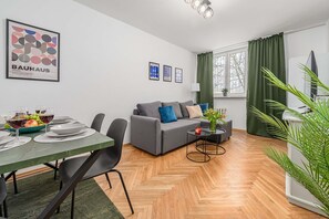Ein modernes Wohnzimmer mit einem grauen Sofa, einem Esstisch mit Tellern und Gläsern sowie einer grünen Pflanze.
