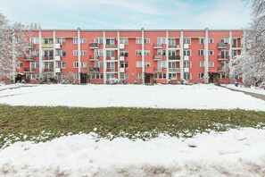 Ein mehrstöckiges Wohngebäude mit Balkonen, einer flachen Dachterrasse und einem schneebedeckten Untergrund.