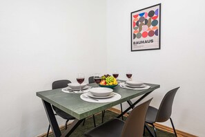 Ein Esstisch mit Geschirr, Besteck und Gläsern, dazu eine Obstschale und ein Bauhaus-Poster an der Wand.