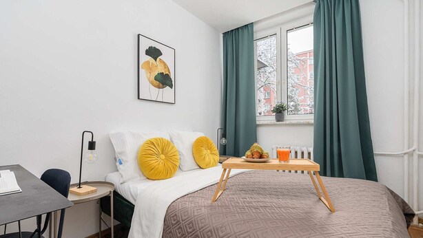A neatly arranged hotel room with a bed, bedside table, lamp, and a window with curtains. - Family Stay on Boguckiego (Warszawa)