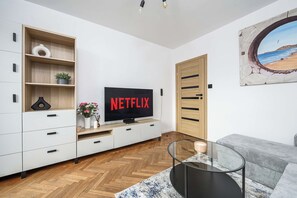 A modern living room with a flat-screen TV, wooden shelving, a sofa, and a glass coffee table. - Old Town Apartment for 4 (Warszawa)