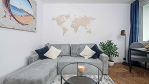 A modern living room with a grey sofa, a glass coffee table, a world map on the wall, and a potted plant. - Old Town Apartment for 4 (Warszawa)