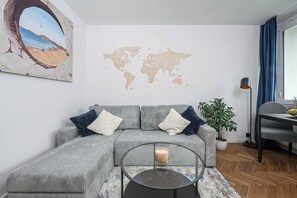 A modern living room with a grey sofa, a glass coffee table, a world map on the wall, and a potted plant. - Old Town Apartment for 4 (Warszawa)
