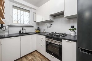 A modern kitchen with white cabinets, a black countertop, a gas stove, and a built-in oven. - Old Town Apartment for 4 (Warszawa)