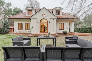 A two-story house with a front porch, a dining area with outdoor furniture, and a well-maintained garden.