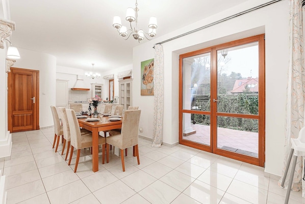 A dining area with a wooden table and chairs, a chandelier, and a large sliding glass door to the outside.