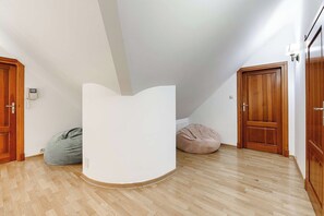 A room with a white, curved partition, wooden flooring, two bean bags, and wooden doors.
