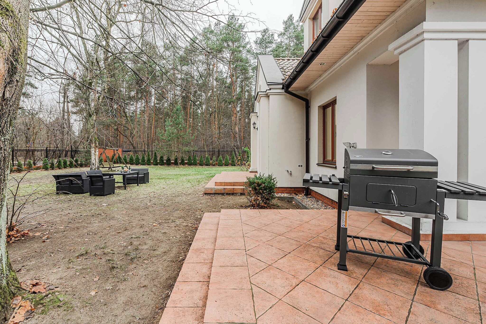 A patio with a grill, outdoor furniture, and a fenced yard with trees.