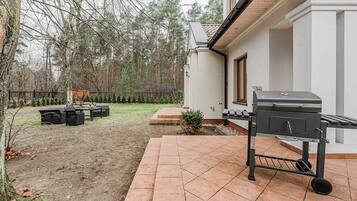 A patio with a grill, outdoor furniture, and a fenced yard with trees.