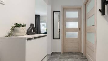 A hallway with a white door, a mirror, and a shelf with decorative items.