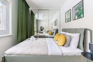 A modern bedroom with a bed, green curtains, a mirror, and artwork on the wall. - Warsay Apartment near Metro (Warszawa 2)