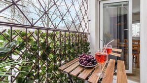 A wooden table with a bowl of grapes and two glasses of red beverage, a metal trellis with green foliage, and a glass door leading to an interior space. - Warsay Apartment near Metro (Warszawa 2)