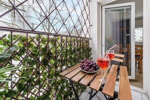 A wooden table with a bowl of grapes and two glasses of red beverage, a metal trellis with green foliage, and a glass door leading to an interior space. - Warsay Apartment near Metro (Warszawa 2)
