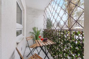 Un petit balcon avec une table en bois, deux chaises, un pot de fleurs et une clôture en métal.