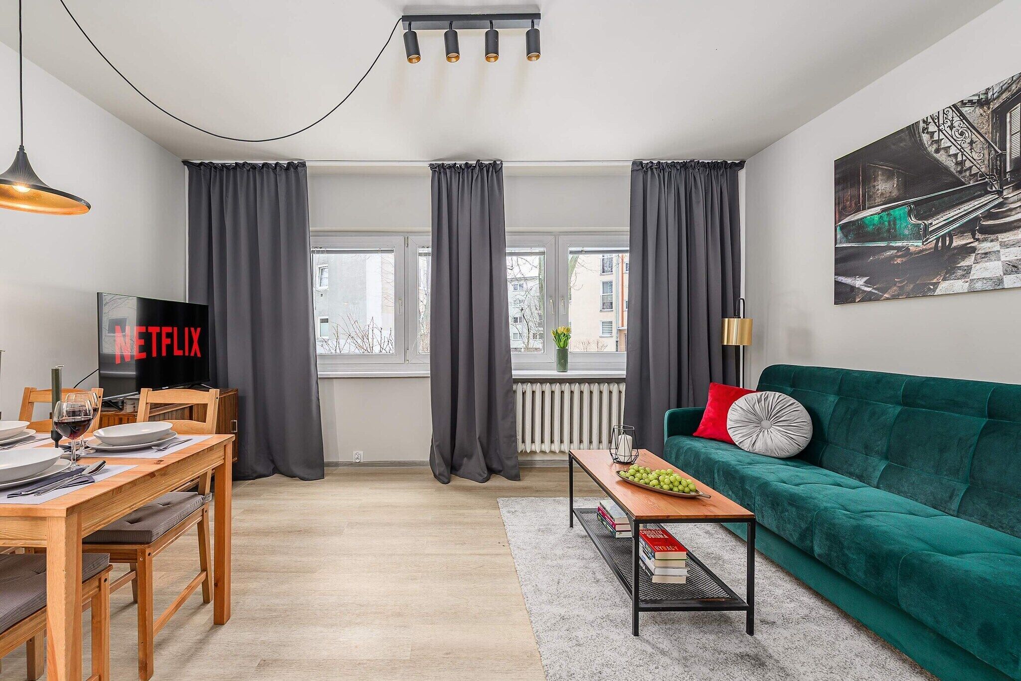 Ett vardagsrum med en grön soffa, ett matbord med stolar, en tv och ett fönster med gardiner.