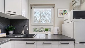 A modern kitchen with a black countertop, white cabinets, a stainless steel sink, a window with a geometric pattern, a white kettle, and a microwave. - Warsay Apartment near Metro (Warszawa 2)