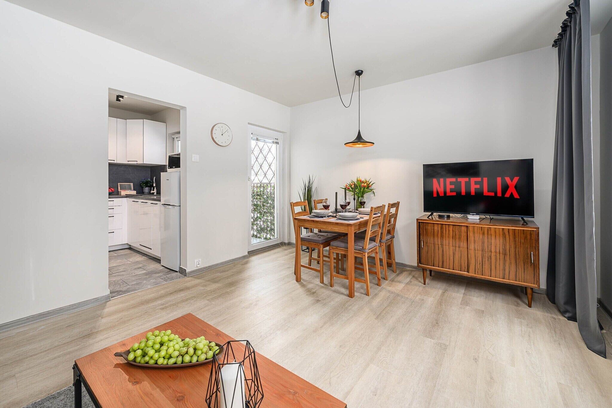 A modern living room with a dining area, a kitchen in the background, and a flat-screen TV displaying 'NETFLIX'.
