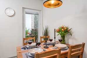 Un coin repas avec une table dressée pour quatre personnes, une horloge au mur et une fenêtre donnant sur un paysage verdoyant.
