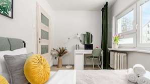 A hotel room with a bed, a desk with a computer, a chair, a window with curtains, and a radiator. - Warsay Apartment near Metro (Warszawa 2)