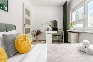 A hotel room with a bed, a desk with a computer, a chair, a window with curtains, and a radiator. - Warsay Apartment near Metro (Warszawa 2)