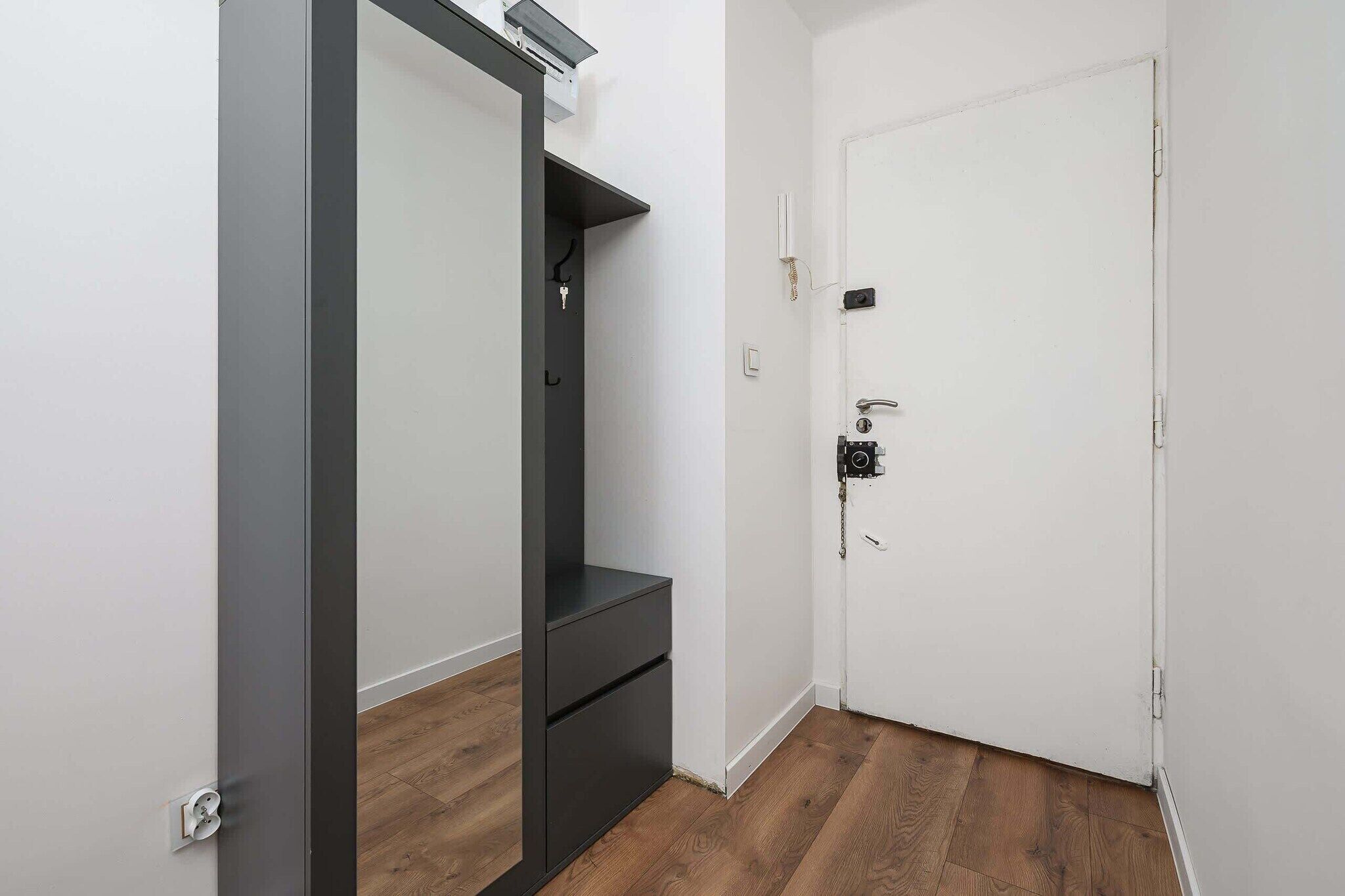A room with a white door, a dark-colored wardrobe, and a wooden floor.