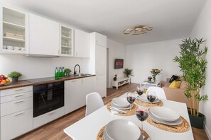 A modern kitchen with white cabinetry, a built-in oven, and a dining area set for a meal with wine glasses and plates. - Warsaw Flat on Pereca (Warszawa 2)