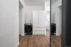 A laundry room with a washing machine and dryer, white cabinets, and wooden flooring. - Warsaw Flat on Pereca (Warszawa 2)