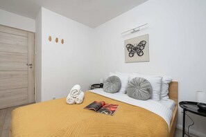 A hotel room with a bed, a wooden door, a wall-mounted light, and a butterfly artwork. - Elegant Apartment with Beautiful City View (Warszawa 2)