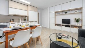 Eine moderne Küche mit weißen Schränken, einem Esstisch mit Stühlen und einem Flachbildfernseher auf einem Regal.