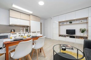 A modern kitchen with white cabinets, a dining table with chairs, and a flat-screen TV on a shelf. - Elegant House with Beautiful Seaview (Warszawa 2)