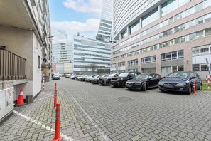A parking area with multiple cars, a cobblestone path, and modern buildings in the background. - Elegant Apartment with Beautiful City View (Warszawa 2)
