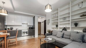 A modern living room with a grey sofa, a wooden dining table, and a kitchen in the background. - Warsaw Flat with Church Views (Warszawa 2)