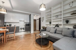 A modern living room with a grey sofa, a wooden dining table, and a kitchen in the background. - Warsaw Flat with Church Views (Warszawa 2)