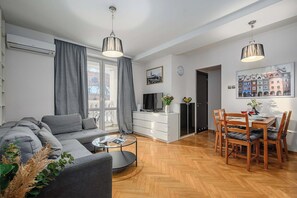 A modern living room with a sofa, coffee table, and dining area with chairs and a table. - Warsaw Flat with Church Views (Warszawa 2)