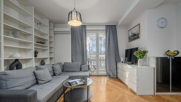 A modern living room with a grey sofa, a glass coffee table, and a TV on a cabinet. - Warsaw Flat with Church Views (Warszawa 2)