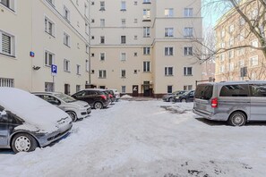 A snow-covered parking area with multiple cars parked in front of a building with multiple windows and balconies. - Warsaw Flat with Church Views (Warszawa 2)