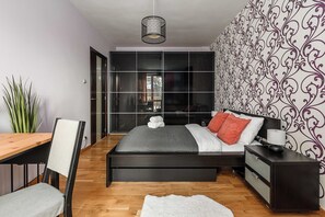 A modern bedroom with a bed, bedside tables, a desk, and a plant. - Warsaw Flat with Church Views (Warszawa 2)