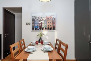 A dining area with a table set for four, chairs, a vase with flowers, and a framed cityscape picture on the wall. - Warsaw Flat with Church Views (Warszawa 2)