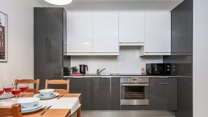 A modern kitchen with grey cabinets, a built-in oven, and a dining area with a wooden table set for two. - Warsaw Flat with Church Views (Warszawa 2)