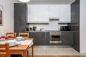 A modern kitchen with grey cabinets, a built-in oven, and a dining area with a wooden table set for two. - Warsaw Flat with Church Views (Warszawa 2)