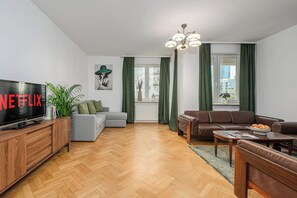 A modern living room with a flat-screen TV, a grey sofa, a brown leather sofa, a wooden TV stand, and a green plant. - Stylish Warsaw Apartment with Balocny (Warszawa 2)