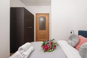 A bedroom with a bed, a wooden wardrobe, a door with a frosted glass panel, and a bouquet of flowers. - Stylish Warsaw Apartment with Balocny (Warszawa 2)