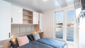A modern bedroom with a bed, built-in shelving, a window with a view of boats, and a ceiling light. - Houseboat With Rooftop Whirlpool in Novigrad (Novigrad)