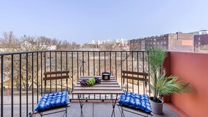 Un balcon avec une table, deux chaises, un saladier de raisins et une plante en pot.
