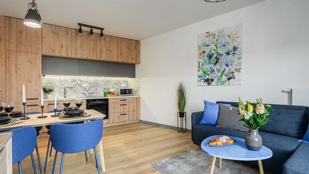 Une cuisine moderne avec des meubles en bois, un coin repas avec des chaises bleues et un salon avec un canapé bleu et une petite table ronde.